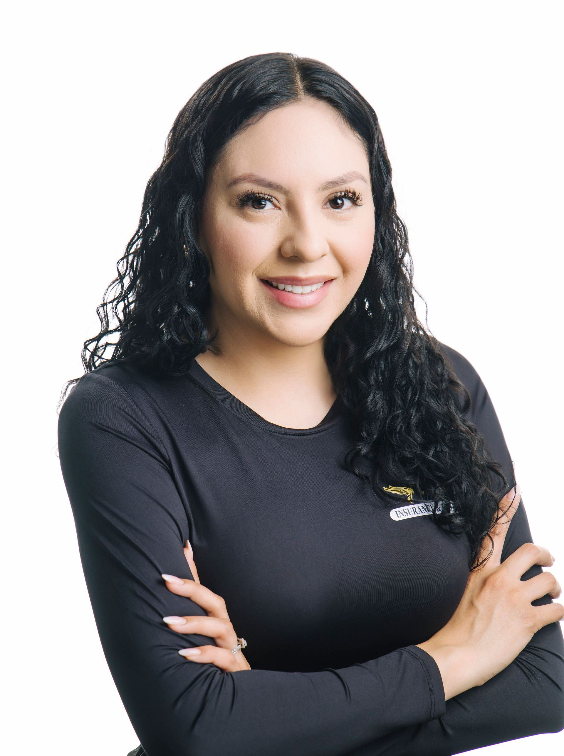 A woman in a red shirt is standing with her arms crossed and smiling.