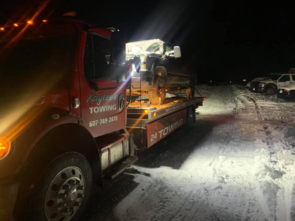 A tow truck is towing a vehicle in the snow at night.