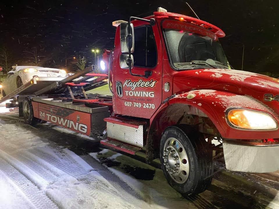A red tow truck is towing a car in the snow.
