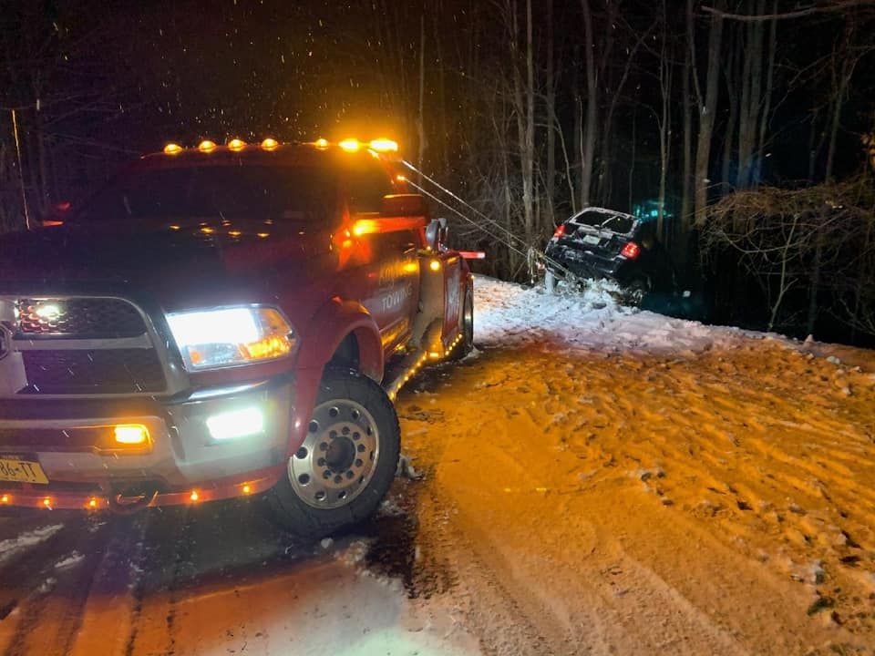 A red truck is towing a car in the snow at night.