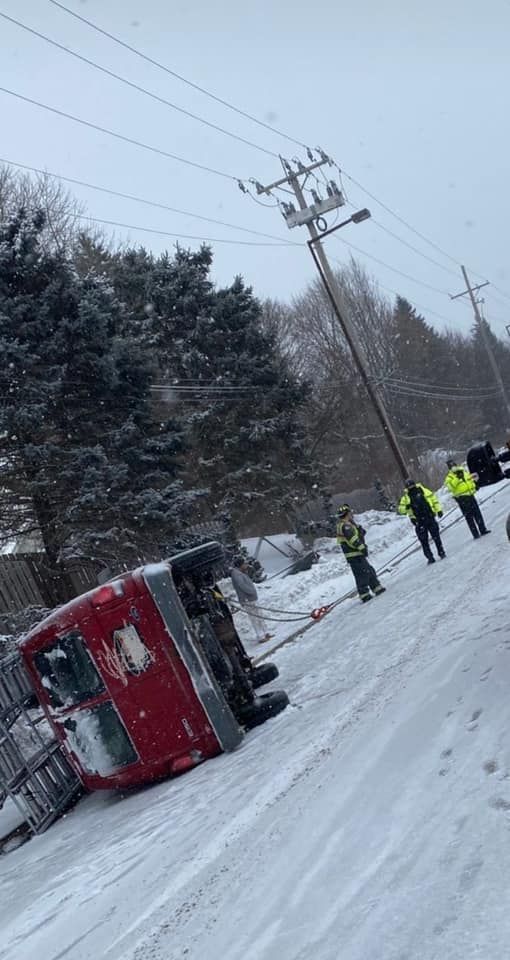 A truck is turned over in the snow on the side of the road.