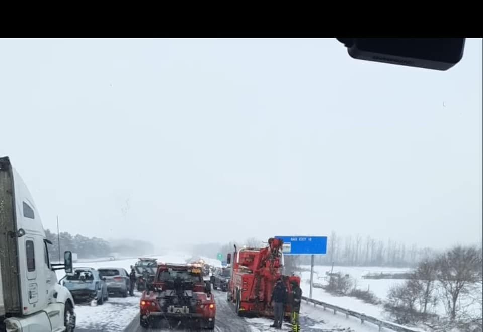 A tow truck is driving down a snowy highway next to a truck.