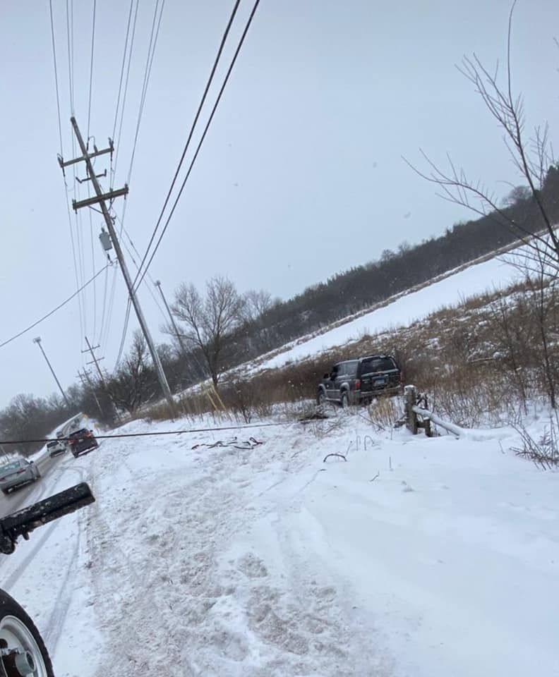 A car is driving down a snowy road next to a power line.