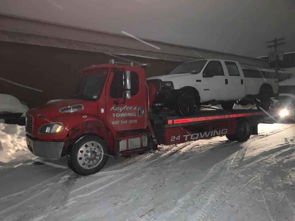 A red tow truck is towing a white truck in the snow.