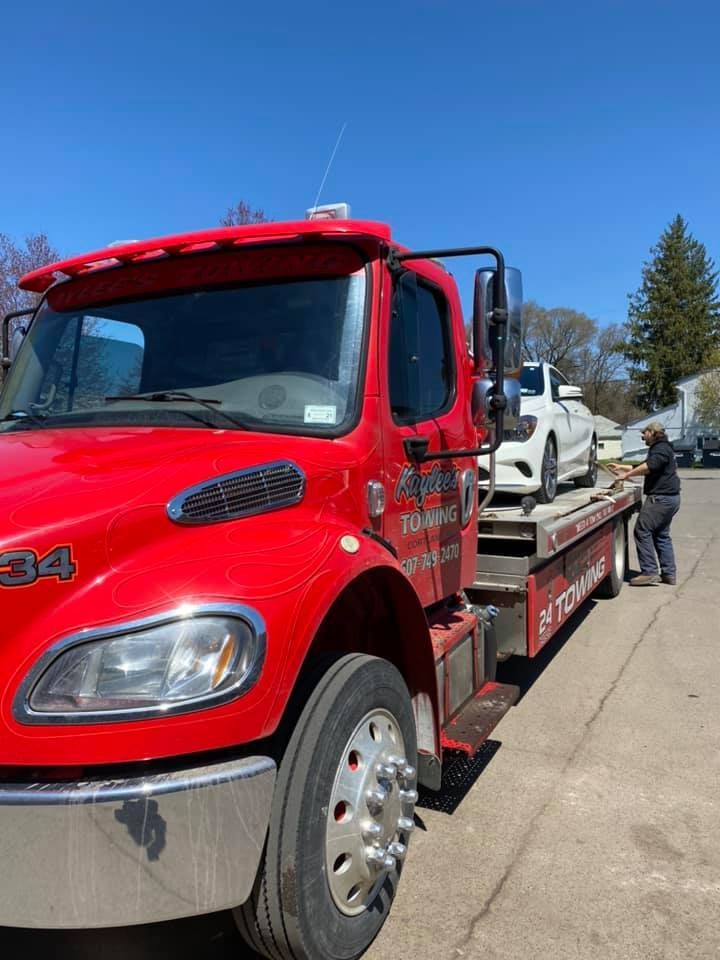 A red tow truck is towing a white car.