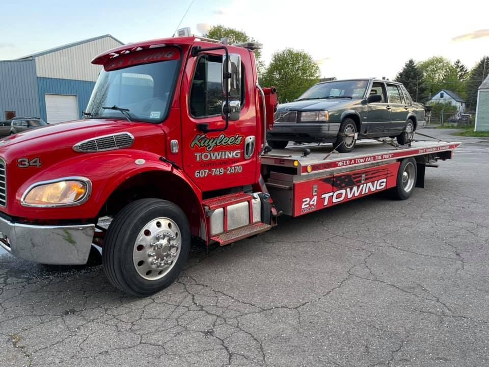 A red towing truck with a car on the back is parked on the side of the road.