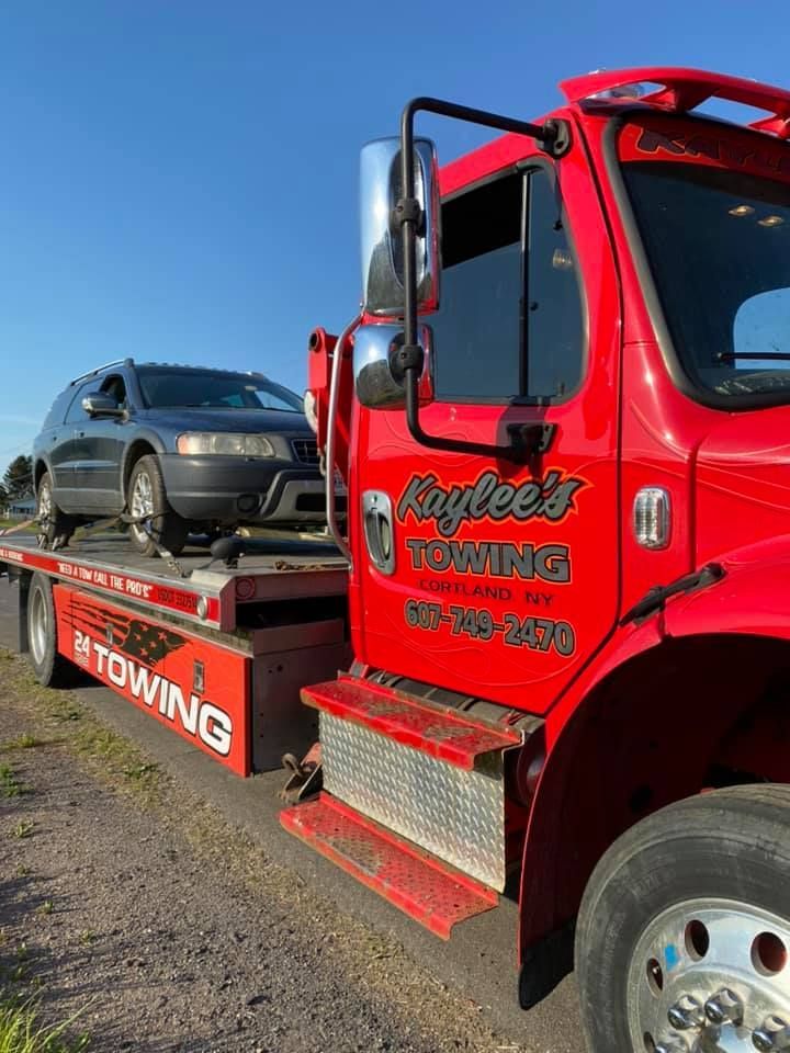 A red towing truck with a car on the back is parked on the side of the road.