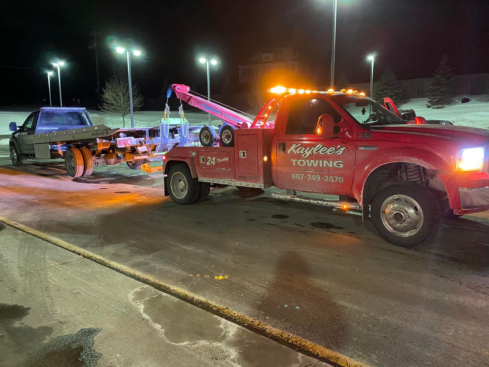 A red tow truck is towing a truck in a parking lot at night.