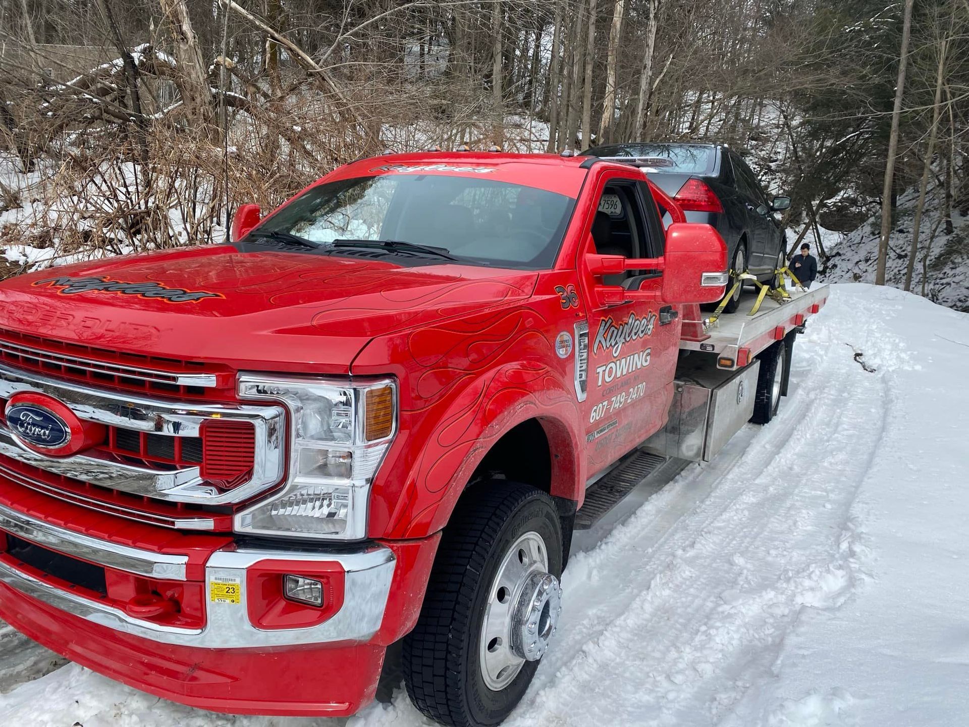 A red tow truck is parked in the snow on a snowy road.