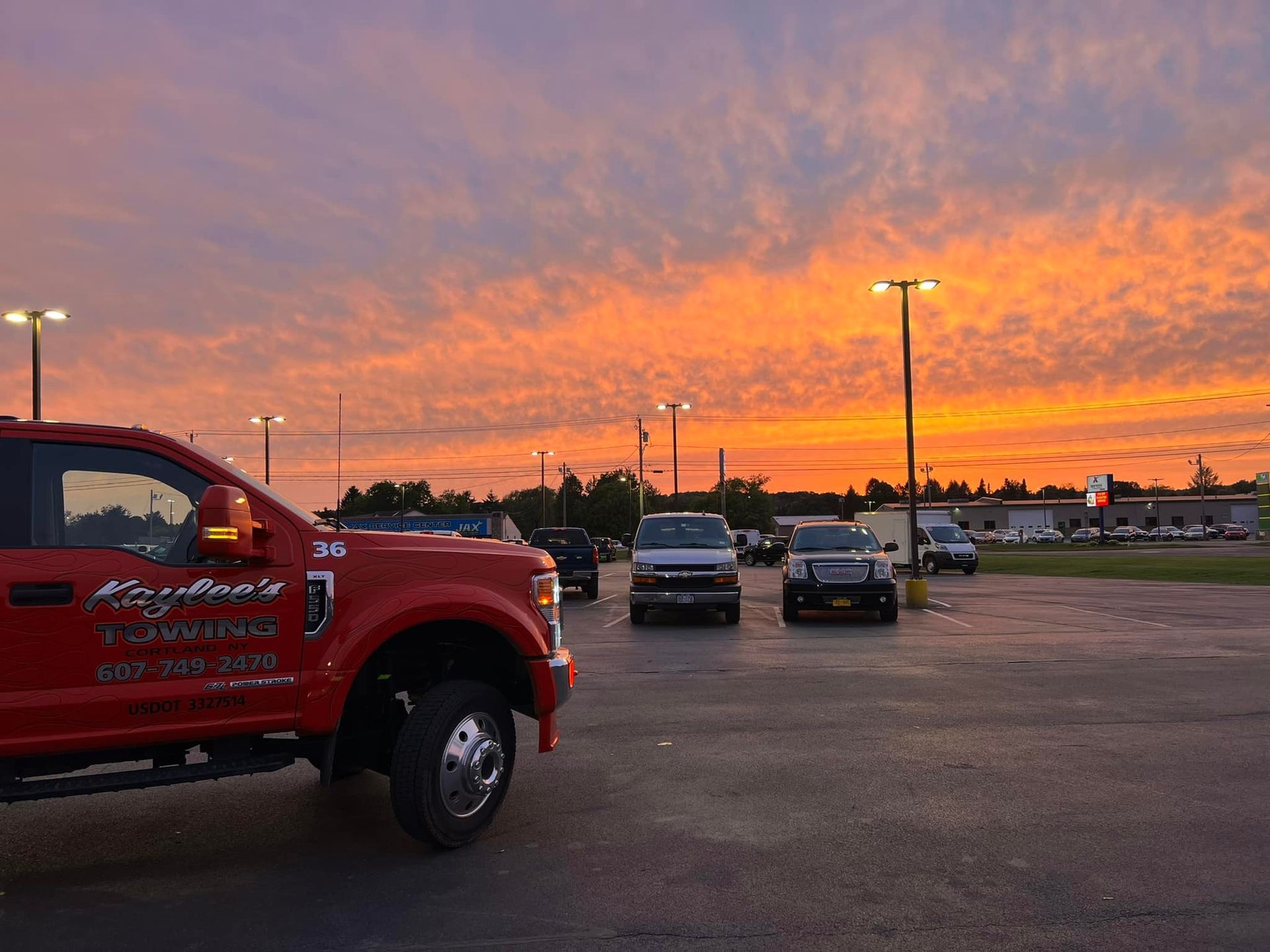 A red truck is parked in a parking lot at sunset.