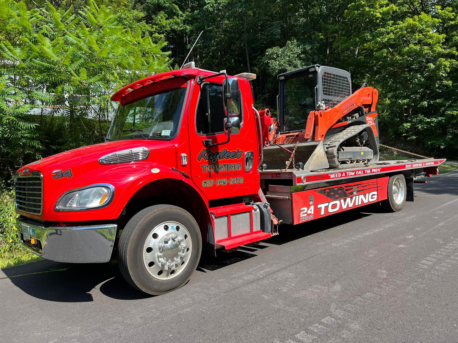 A red towing truck with a bulldozer on the back is parked on the side of the road.