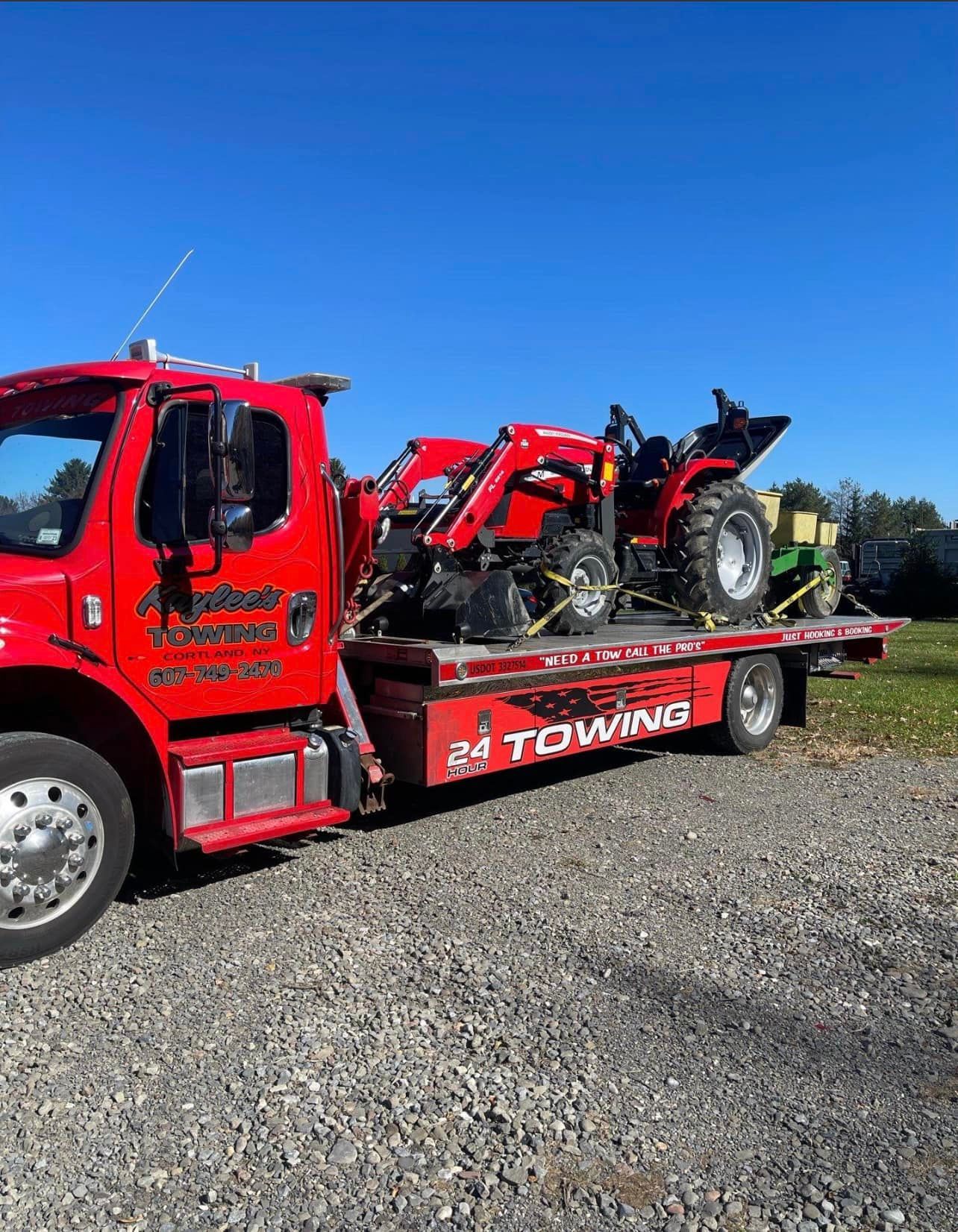 A red towing truck is carrying a tractor on a flatbed trailer.