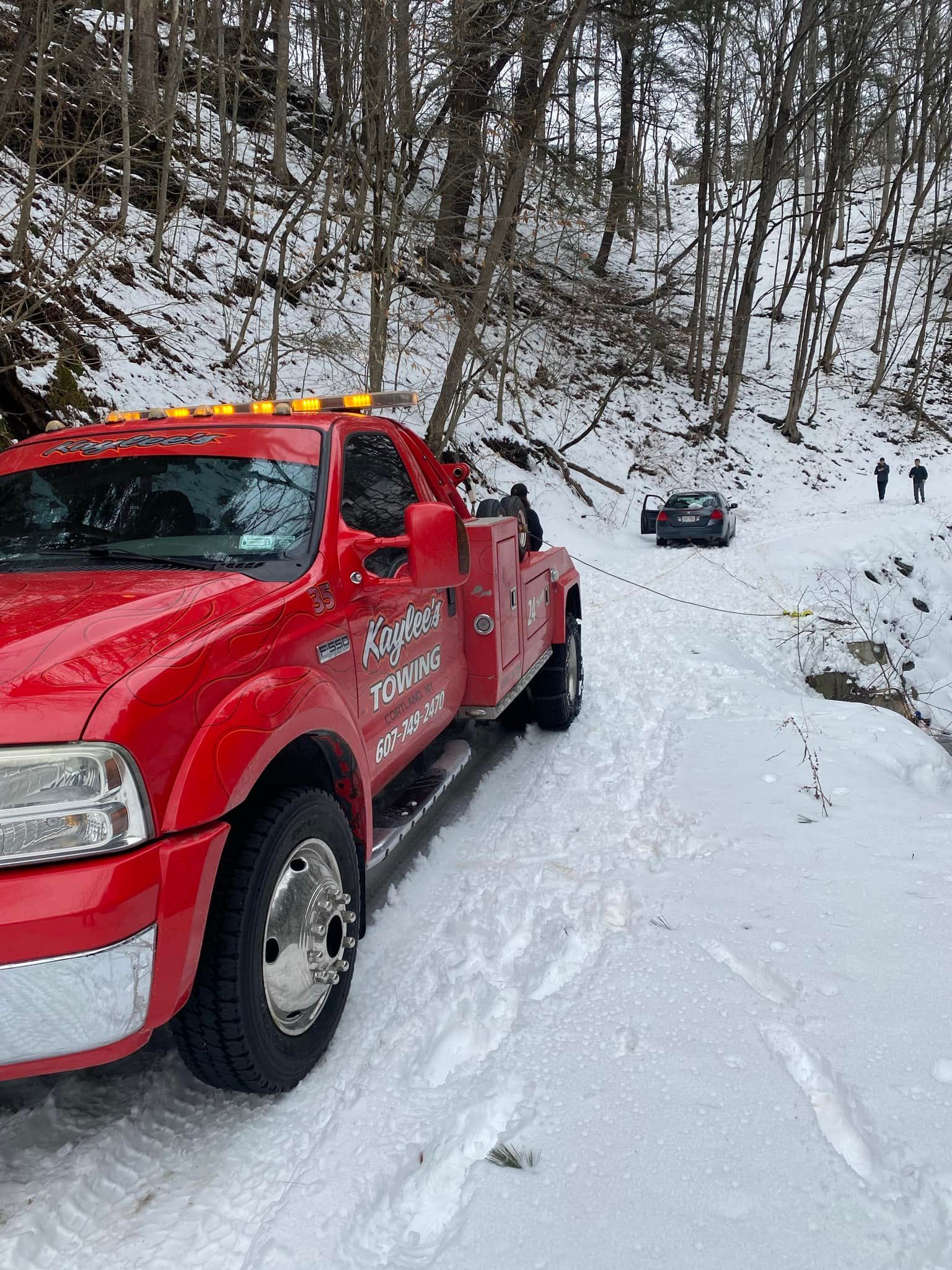 A red tow truck is parked in the snow on a snowy road.