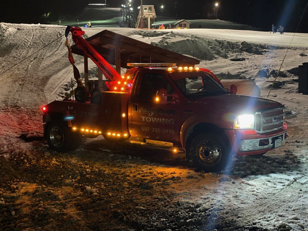 A red tow truck is parked in the snow at night