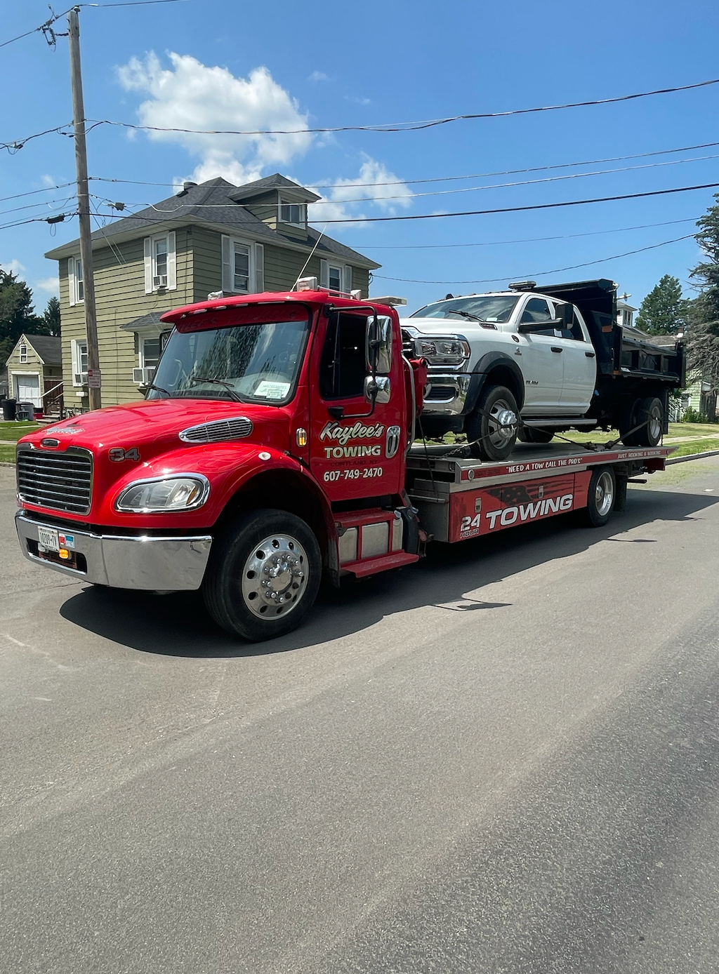 A red tow truck is towing a white truck down a street.