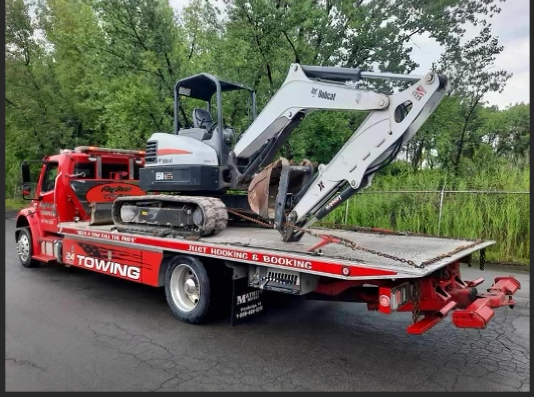 A bobcat excavator is sitting on top of a tow truck.