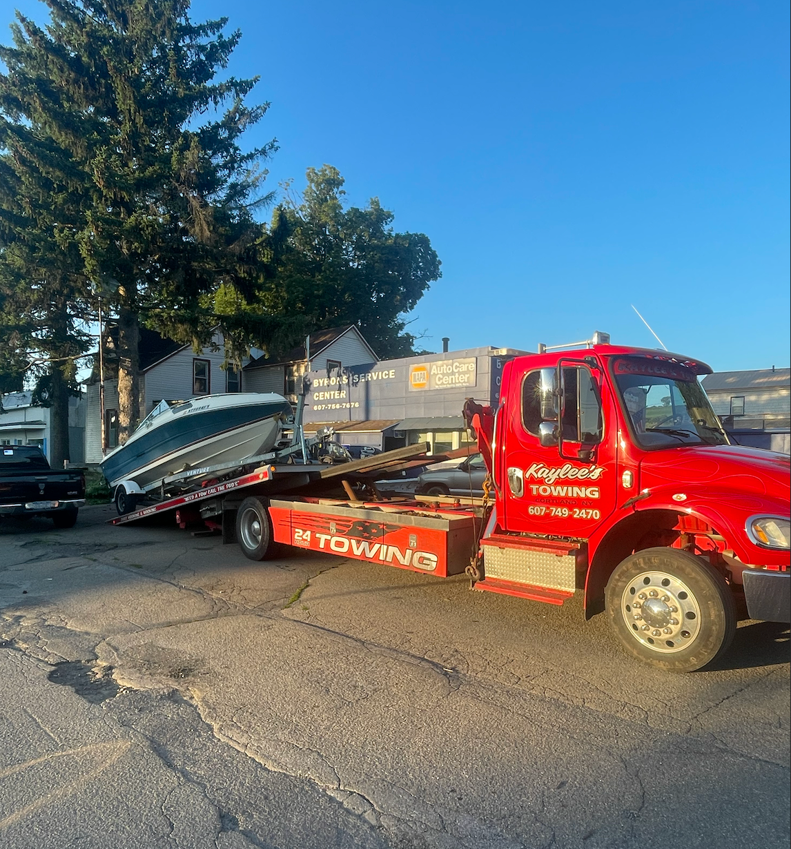 A red tow truck is carrying a boat on the back of it.