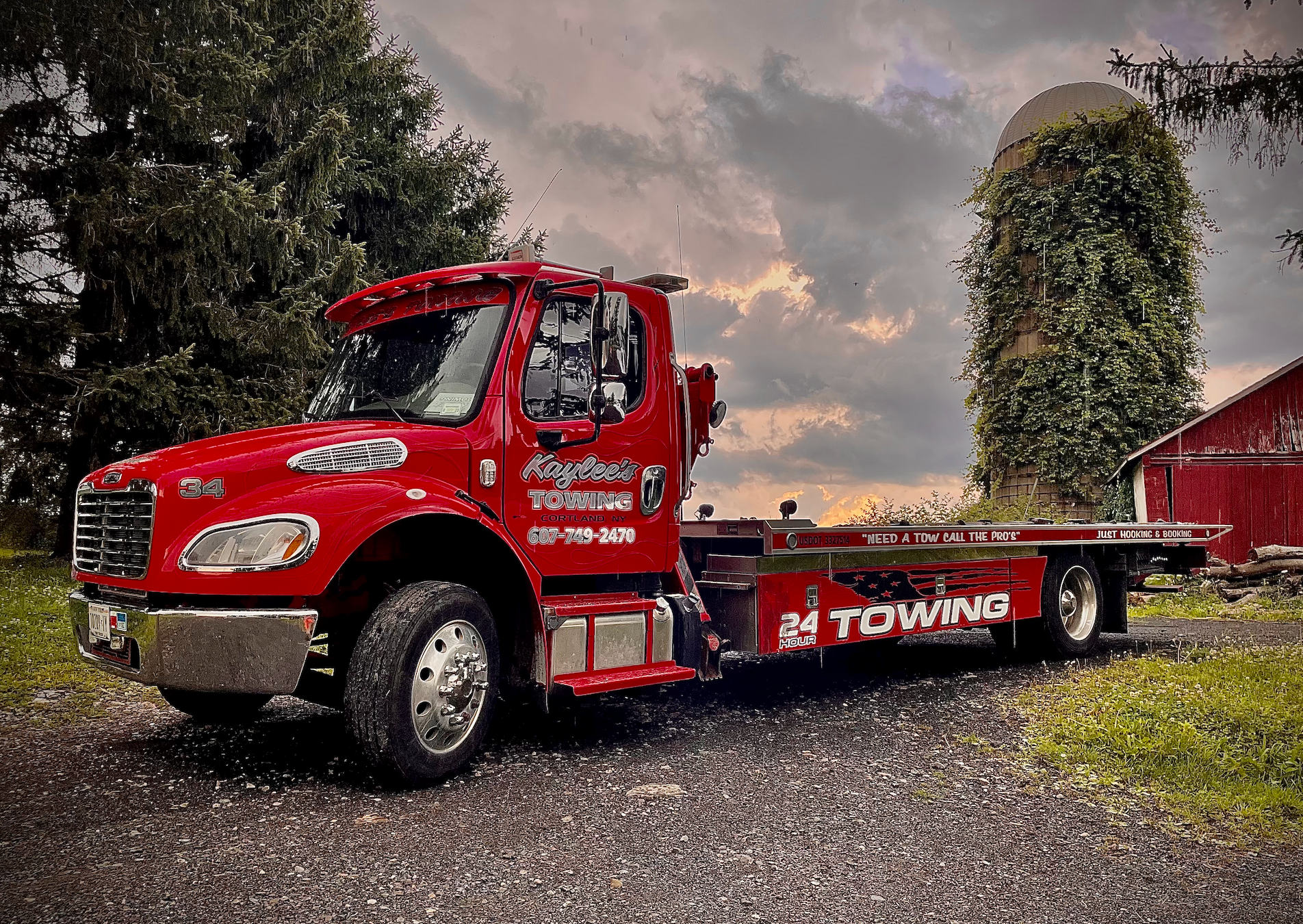 A red towing truck is parked in front of a red barn.