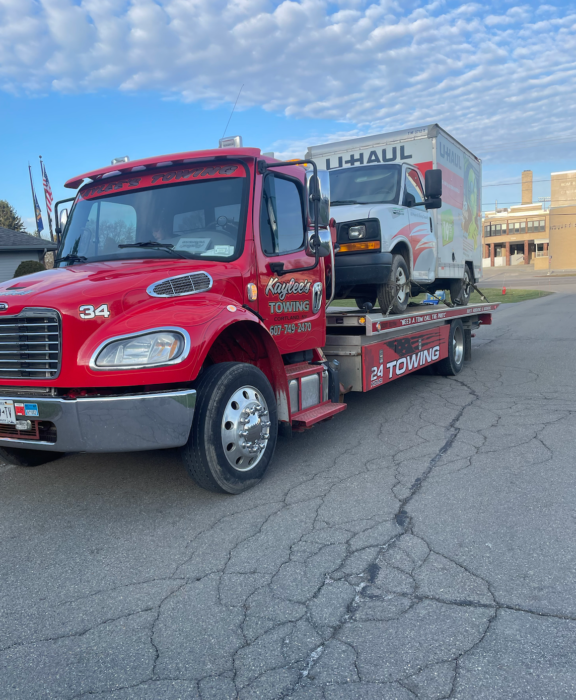 A red tow truck is carrying a white truck and a uhaul box.