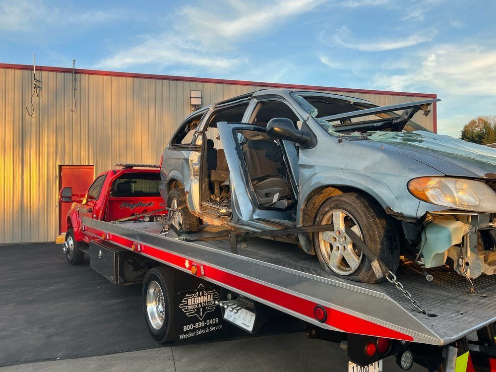 A tow truck is carrying a broken down minivan.