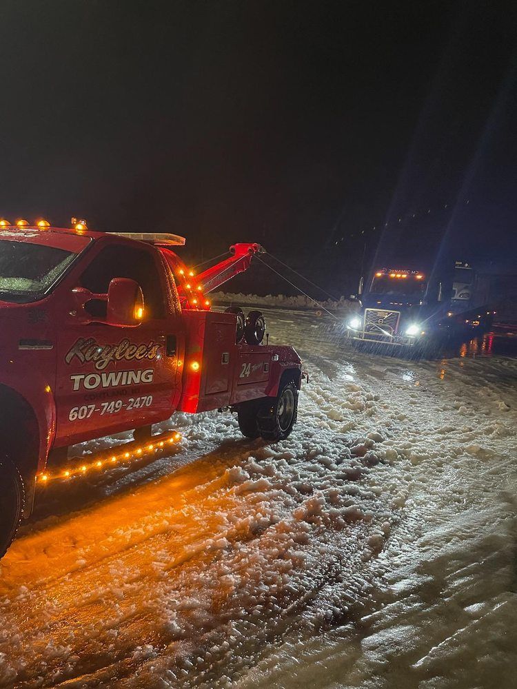 A red tow truck is driving down a snowy road at night.