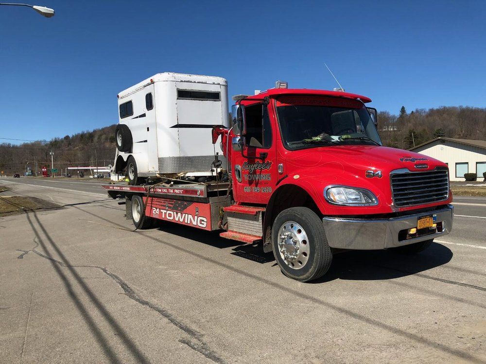 A red tow truck is carrying a white horse trailer.