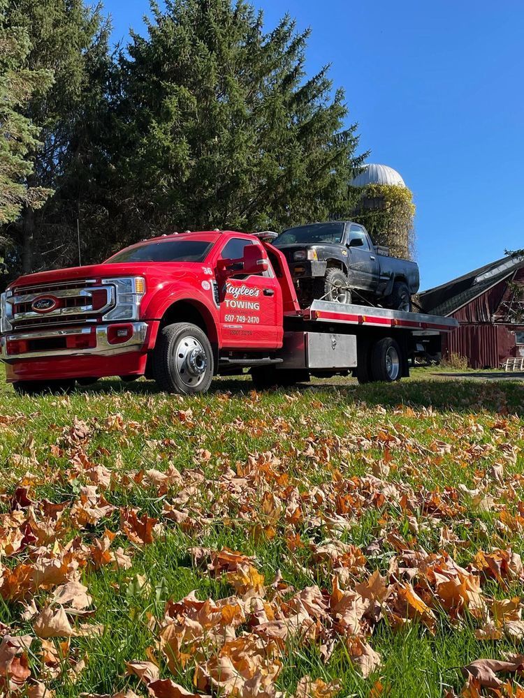 A red tow truck with a car on the back is parked in a field of leaves.