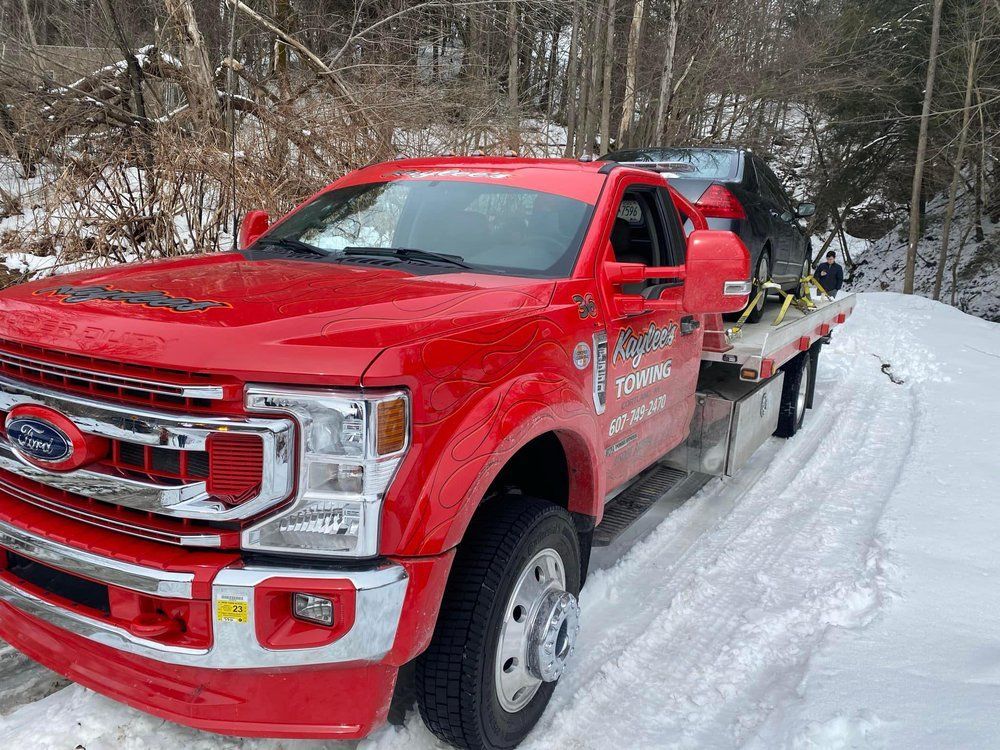 A red tow truck is towing a car in the snow.