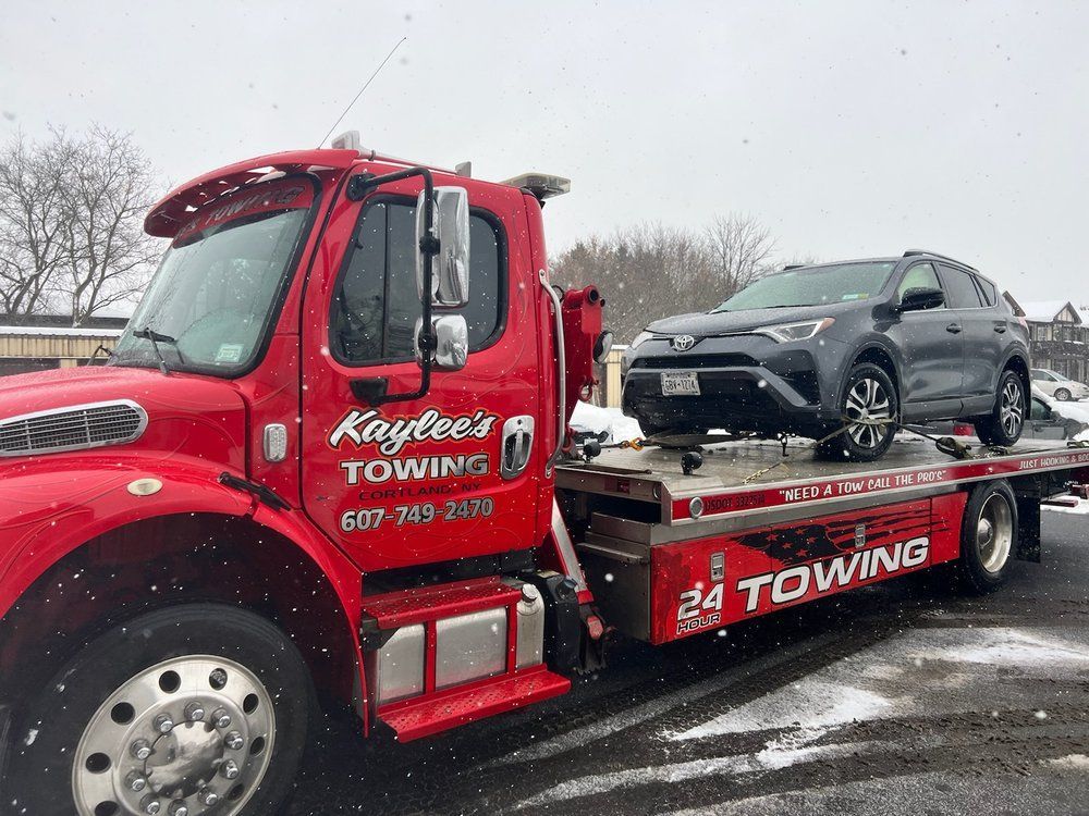 A red towing truck is towing a gray suv in the snow.
