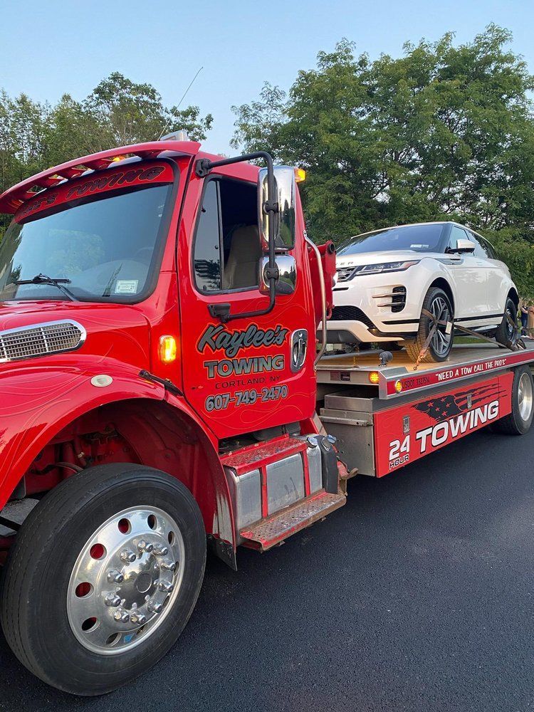 A red tow truck is towing a white car.
