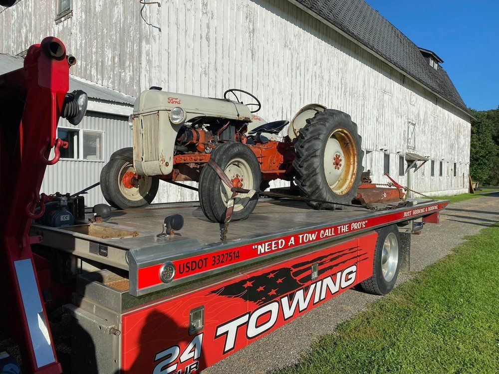 An old tractor is sitting on top of a towing truck.