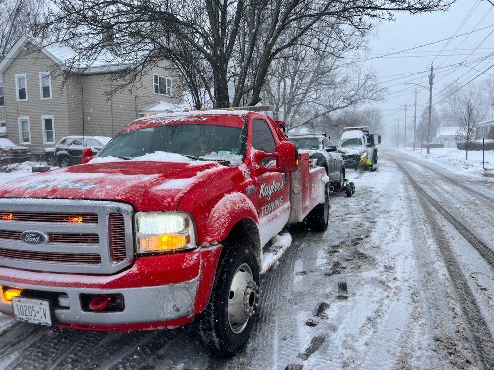 A red tow truck is driving down a snowy street.