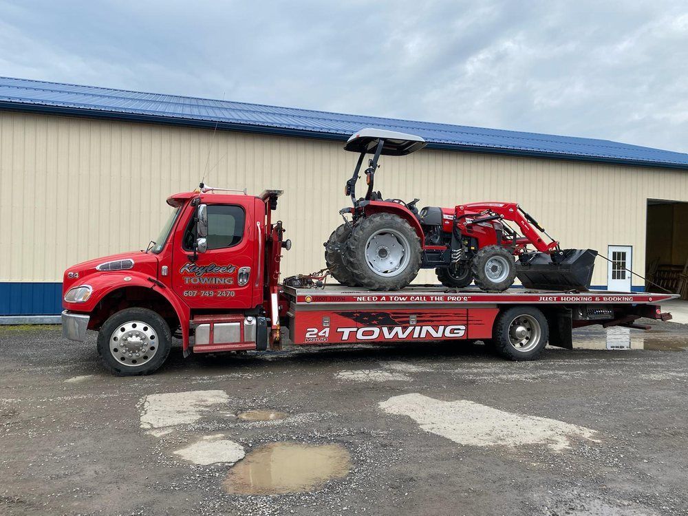 A red towing truck with a tractor on the back is parked in front of a building.