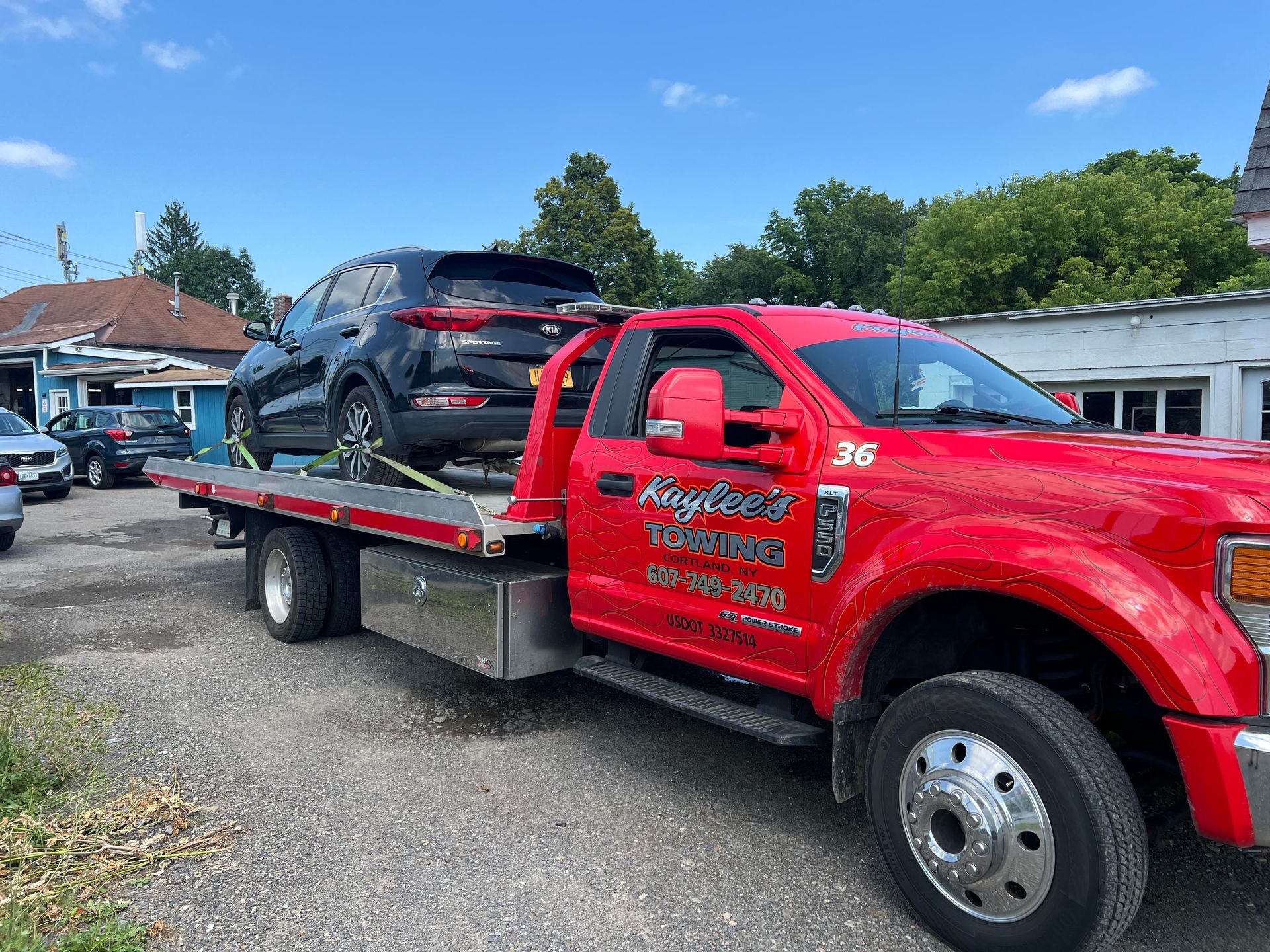 Red tow truck carrying a black SUV on a sunny day. The truck has 
