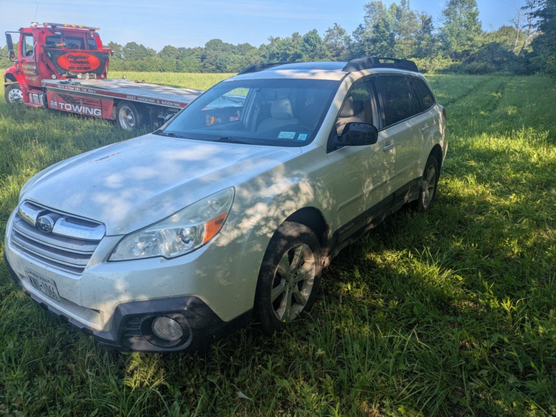 A white suv is parked in a grassy field next to a tow truck.
