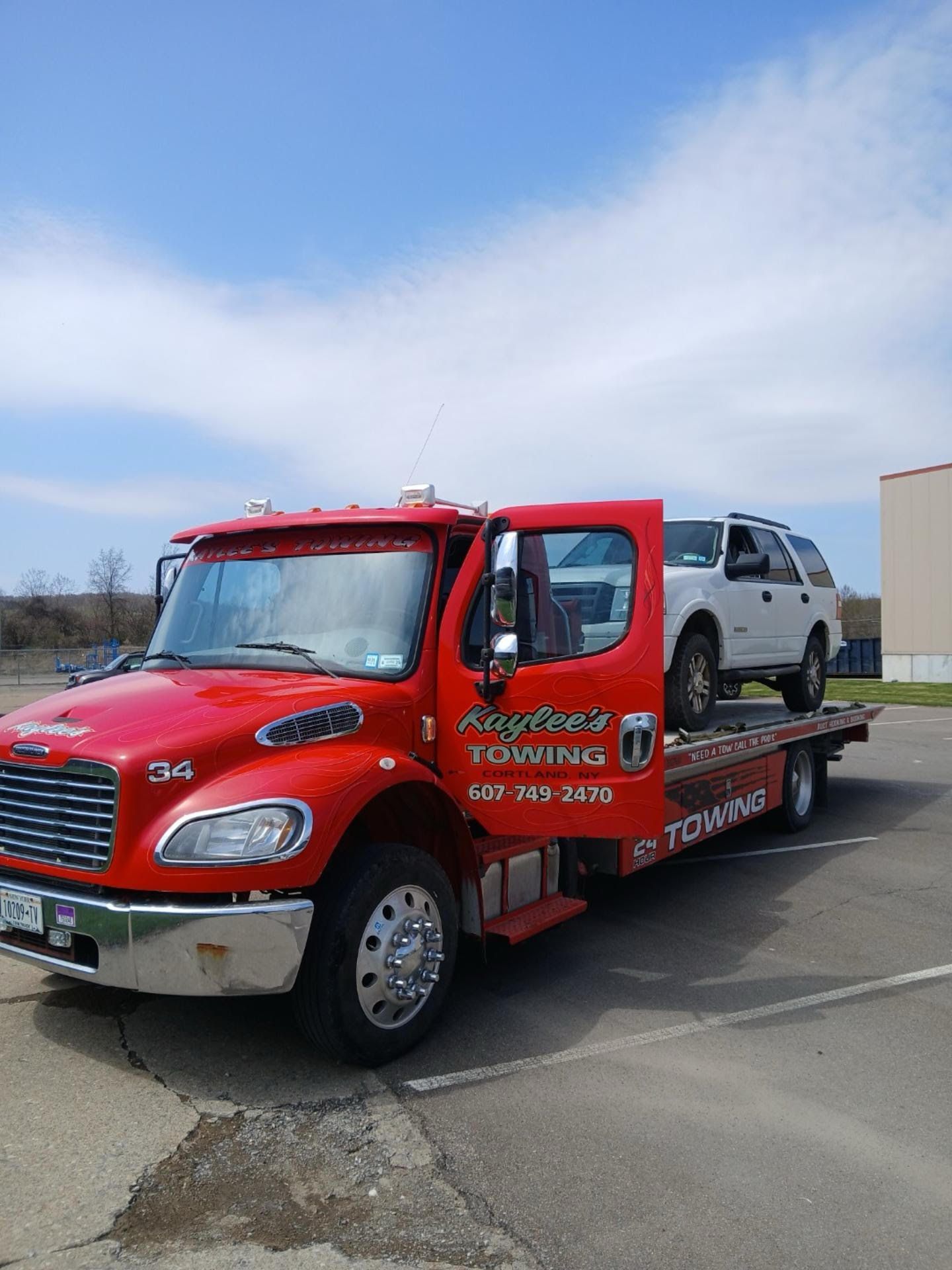 A red tow truck with a white suv on the back is parked in a parking lot.