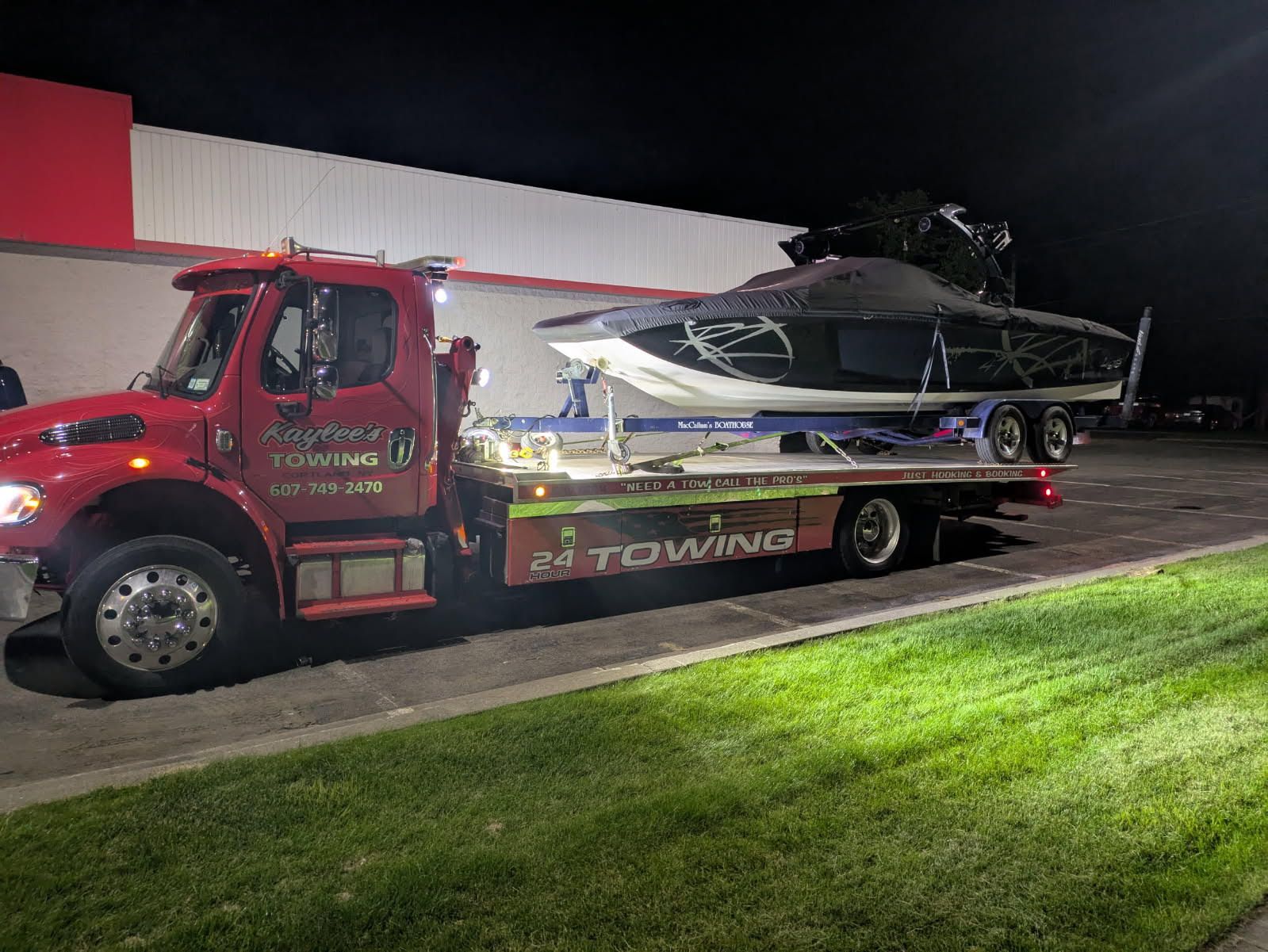 A towing truck is carrying a boat on the back of it.
