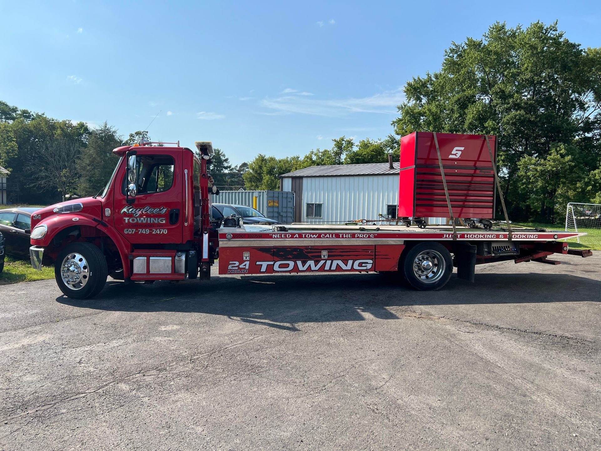 Red tow truck with its flatbed carrying a stack of red objects; parked outside on a sunny day.