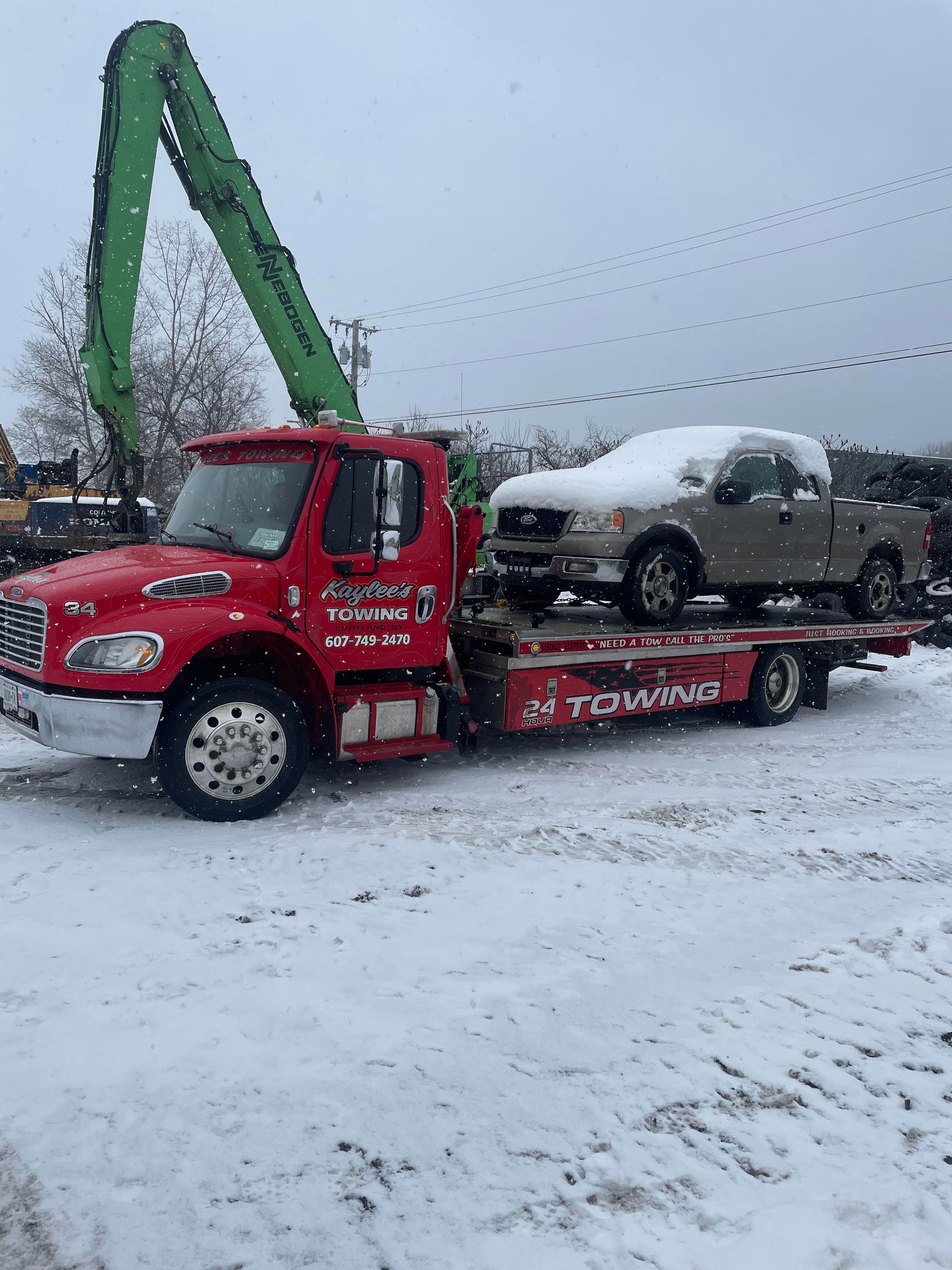 A red tow truck is carrying two cars in the snow.