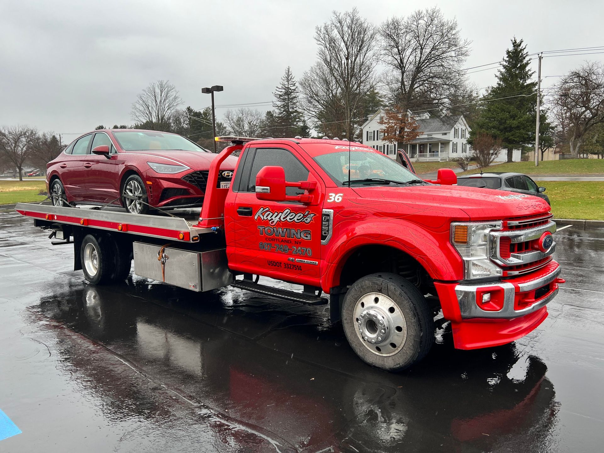 A red tow truck is towing a red car in a parking lot.