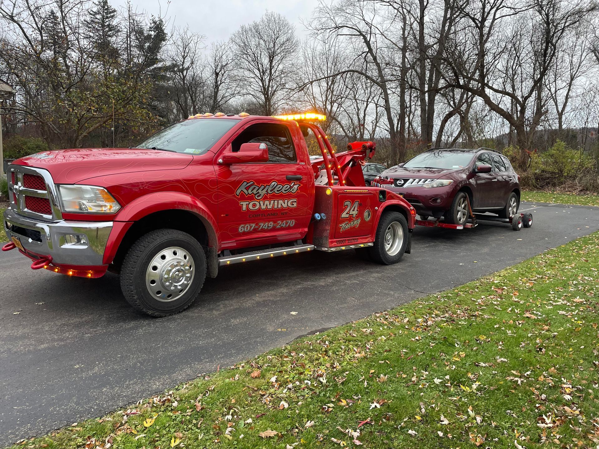 A red tow truck is towing a car down a road.