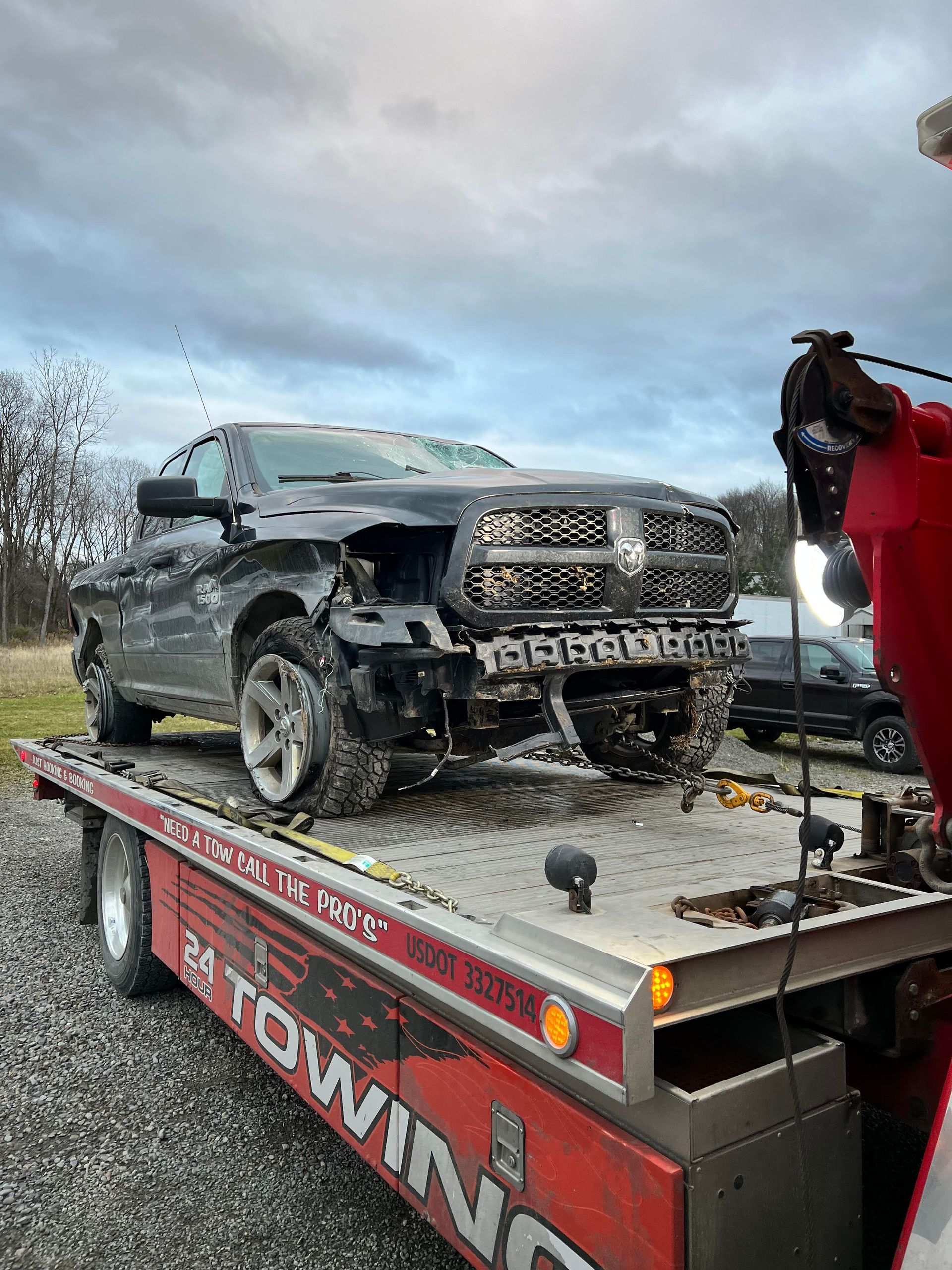 Damaged black pickup truck loaded on a red tow truck.