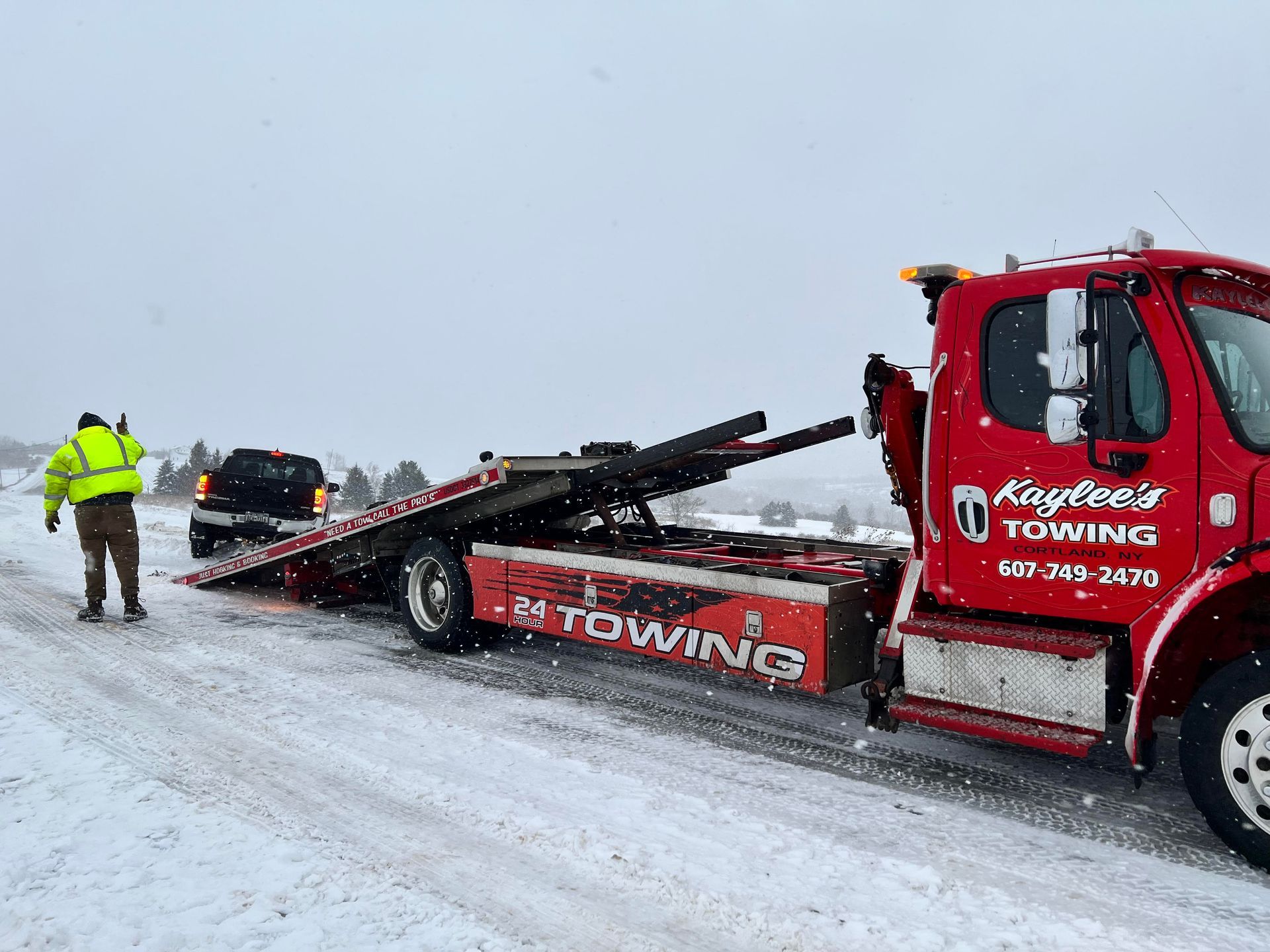 A red towing truck is driving down a snowy road.