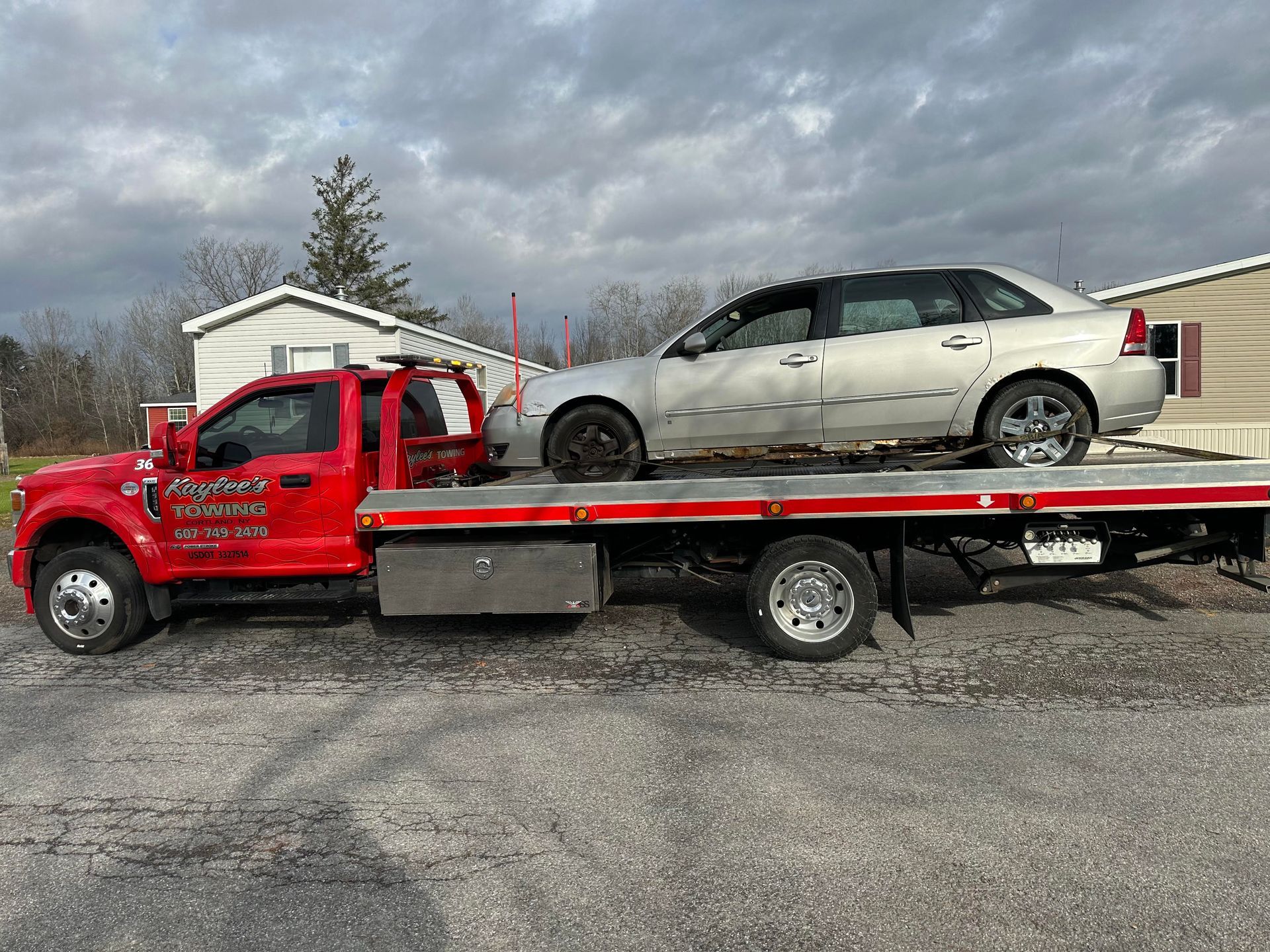 A red tow truck is towing a white car.