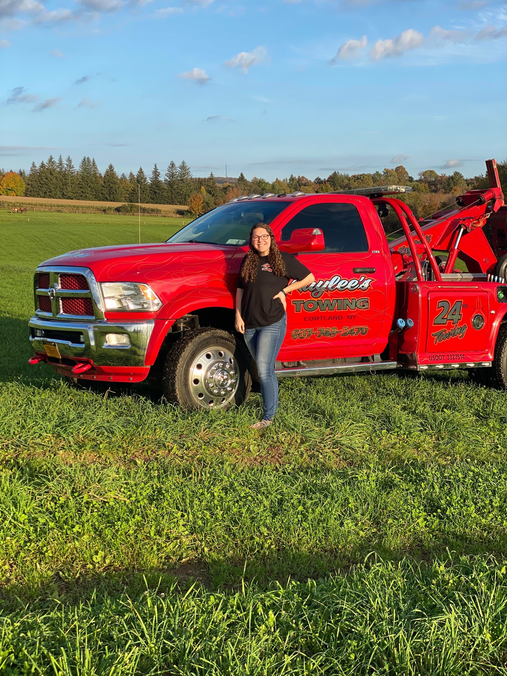 A woman is standing next to a red tow truck in a grassy field.
