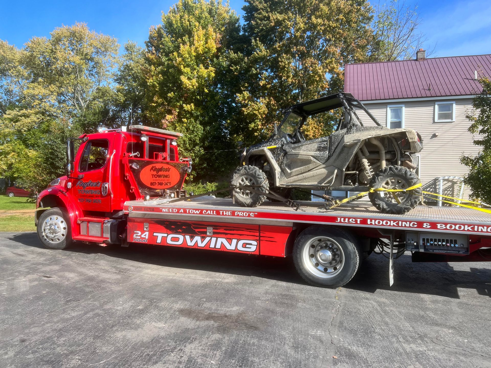 A red towing truck is carrying a atv to a house.