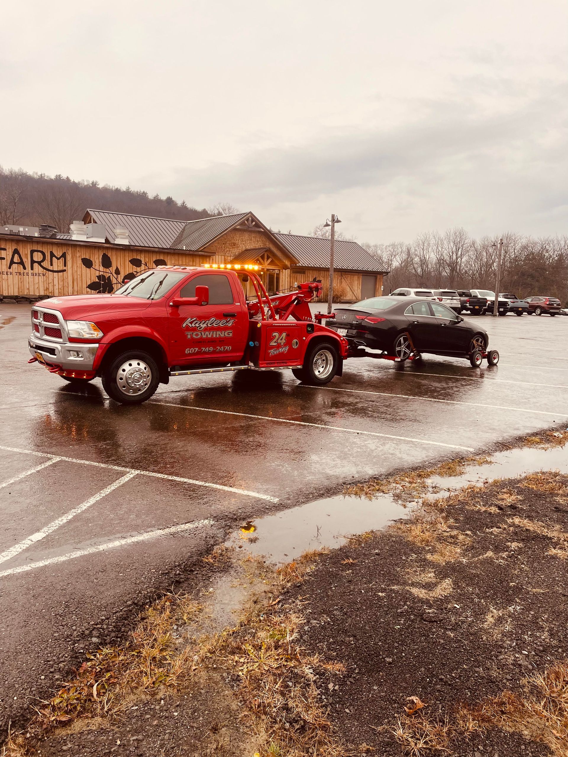 A red tow truck is towing a black car in a parking lot.