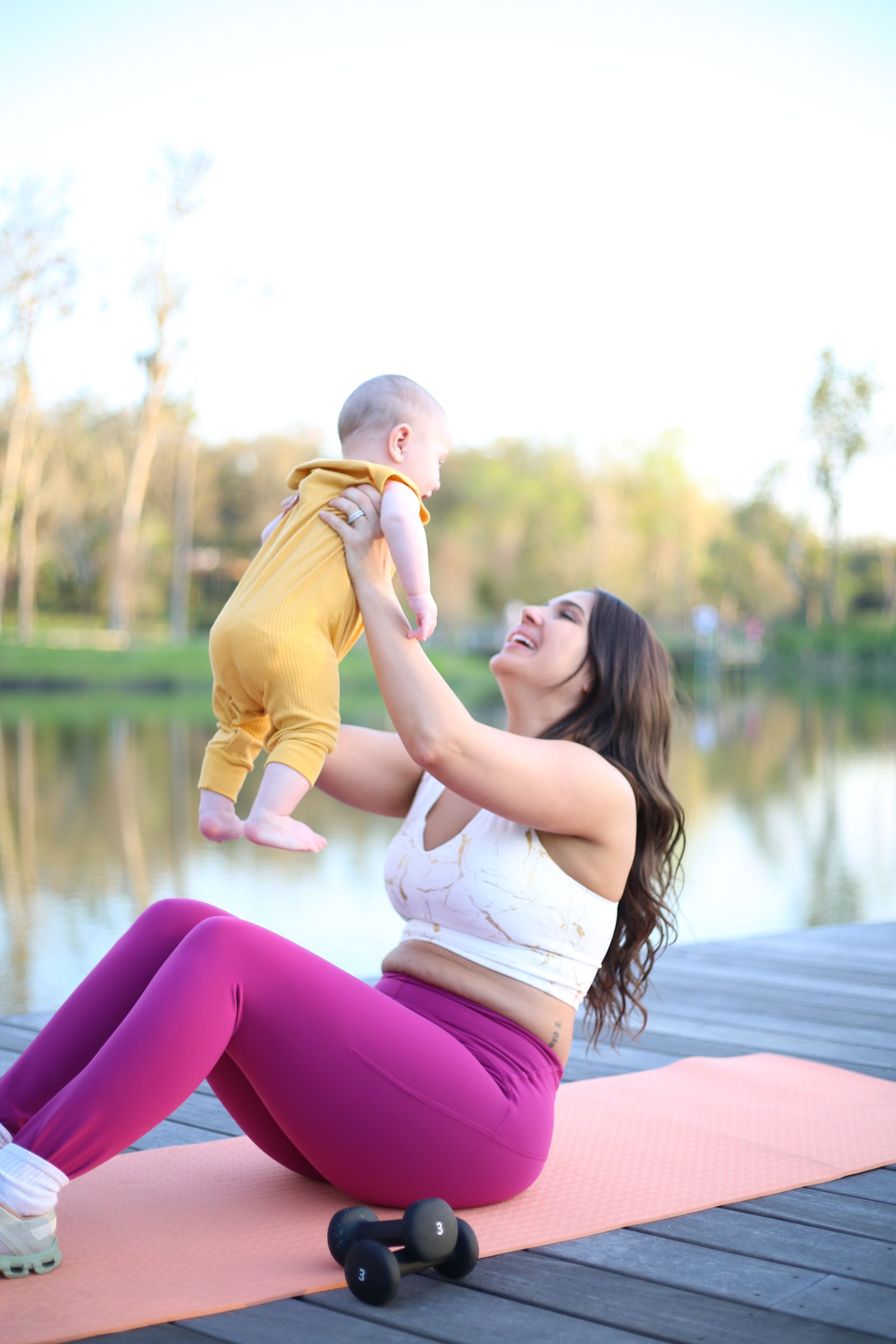 A woman is sitting on a yoga mat holding a baby.