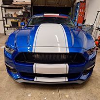 A blue mustang with white stripes is parked in a garage.
