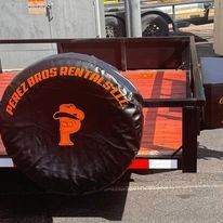 A trailer with a tire cover on it is parked on the side of the road.
